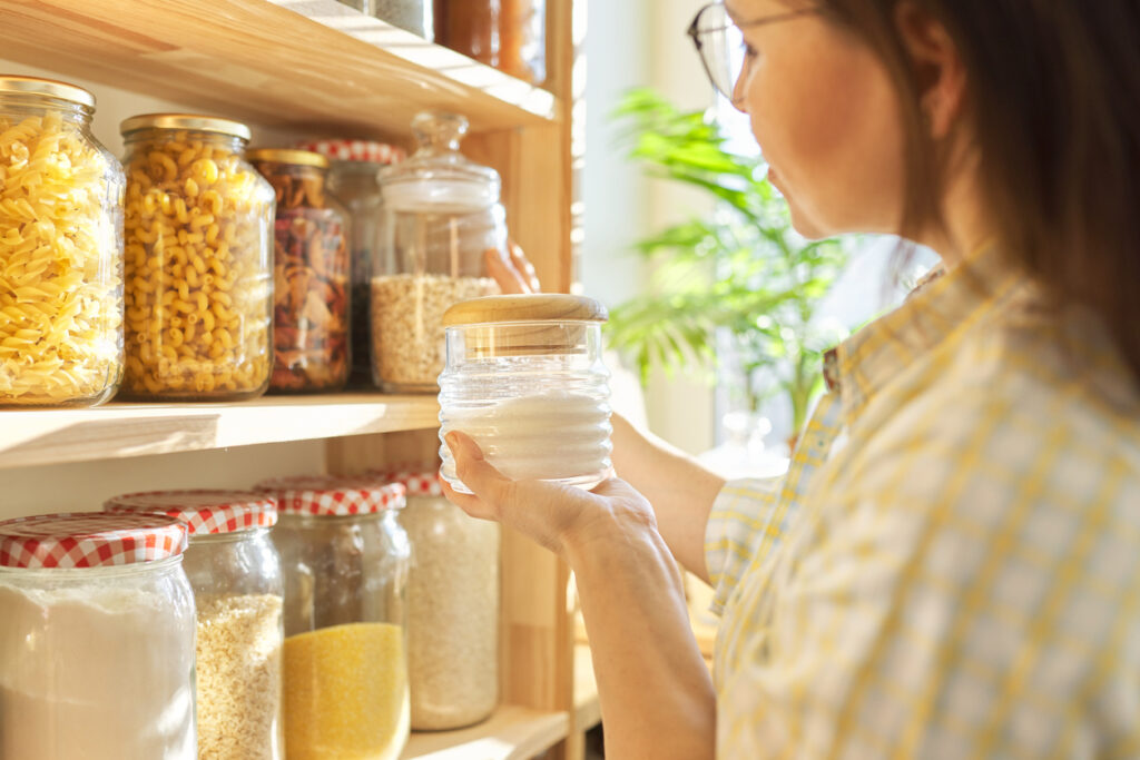 Food storage in pantry, woman holding jar of sugar in hand.